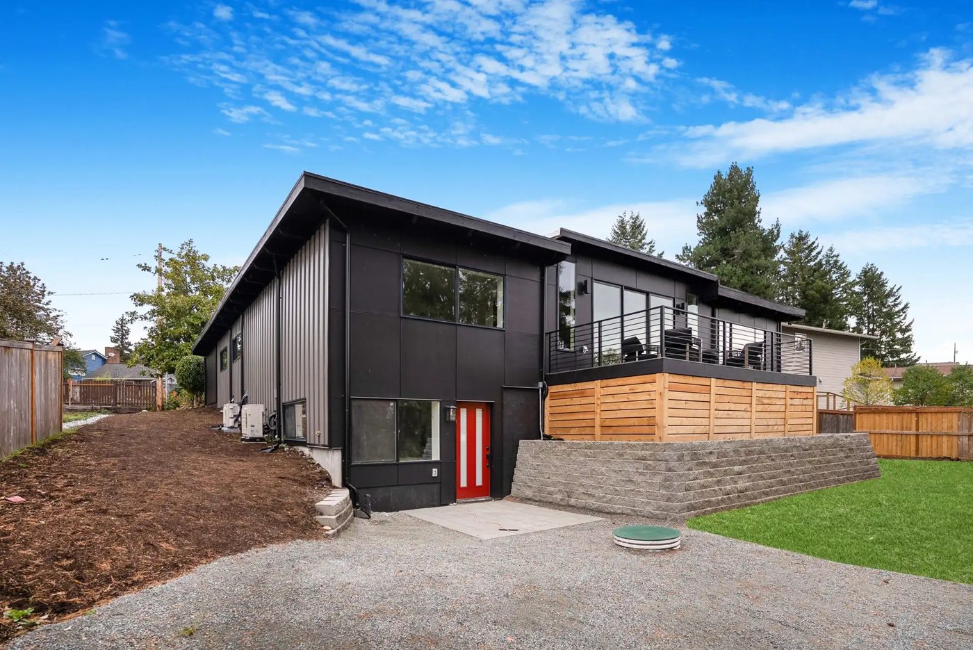 Black modern house on Beacon Hill with a red door at garden level, the entry to the attached studio, below a deck